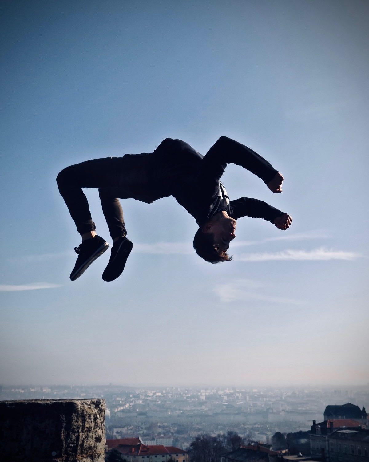Pratiquant de parkour en plein salto au-dessus des toits de Lyon, vu depuis les hauteurs de Fourvière